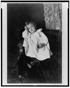 [African American girl, full-length portrait, seated in chair, head resting on right hand, facing front]