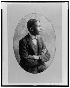 [Young African American man, half-length portrait, seated with arms crossed, right profile]
