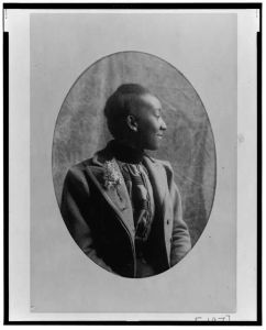 [African American woman, half-length portrait, seated, right profile, wearing coat]