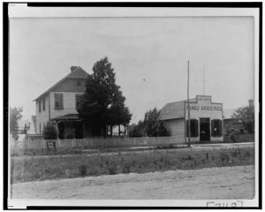 [House with picket fence next to "Lee Bros. Family Groceries"]