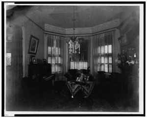 [Interior view of room showing furniture, piano, and chandelier]