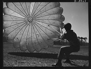 Fort Benning. Parachute troops. Picture of a man doing a good job. He's one of Uncle Sam's student paratroopers at Fort Benning, Georgia, but the way he's getting his chute under control would be credit to an oldtimer. A few minutes ago this man bailed out of a high-speed plane at a point calculated to bring him to the spot where he is landing. Good work, soldier