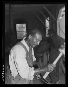 [Untitled photo, possibly related to: Negro farmer sharpening plow points at a new vocational school in Greene County, Georgia]