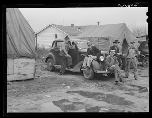 Men on car by tents. Construction workers in front of tents. Names: William Allen Jones, Fort Benning, Paul Knight, Fort Benning, J.F. Goza, C.D. Brownlee and B.I. Juhan. For space only in W.T. Mullis' backyard they pay two dollars a week. Two of them are now working at Fort Benning and others the Williams Construction Company, building foundations for new barracks, got laid off couple of weeks ago for indefinite time. They all came from Stone Mountain, Atlanta, Georgia, where they worked on WPA (Work Projects Administration). Some have been here one month. One said "There's something crooked in this here job--some men have worked every day seven days a week and others get no work at all. It's a dirty shame and the government ought to know about these conditions and see what goes on. It's awful bad."