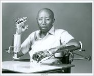 Photograph of an African American male patient wearing hand splints while seated in a wheelchair with mobile arm supports and a lapboard at the Georgia Warm Springs Foundation, Warm Springs, Meriwether County, Georgia, 1971