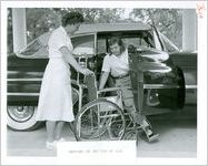 Photograph of a young woman transferring from an automobile to a wheelchair with the help of a female physical therapist at the Georgia Warm Springs Foundation, Warm Springs, Meriwether County, Georgia, 1955