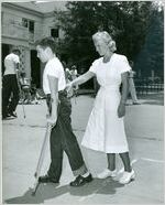 Photograph of a physical therapist supporting a young patient as he practices walking with crutches outdoors at the Georgia Warm Springs Foundation, Warm Springs, Meriwether County, Georgia, 1955-1965?